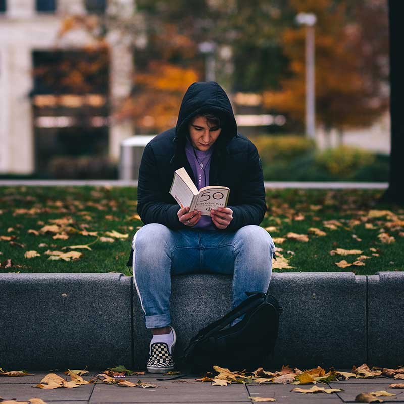 A young person sitting on a wall reading