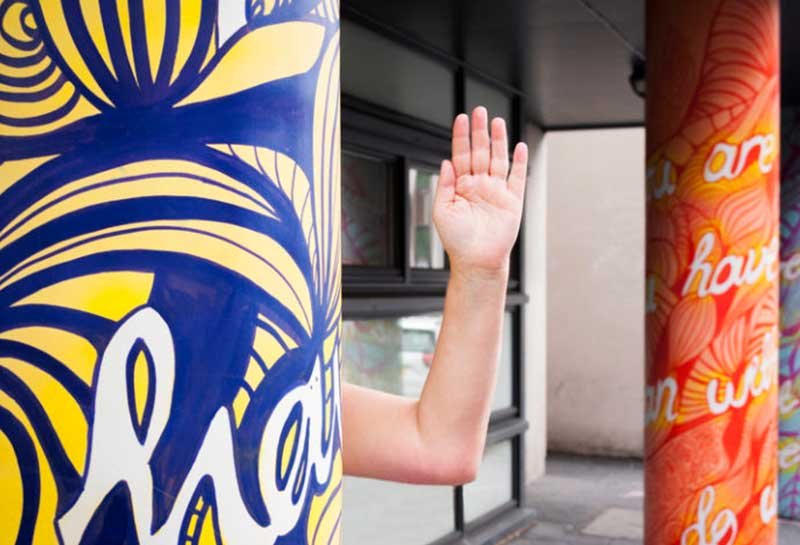 A hand waving from behind a pillar