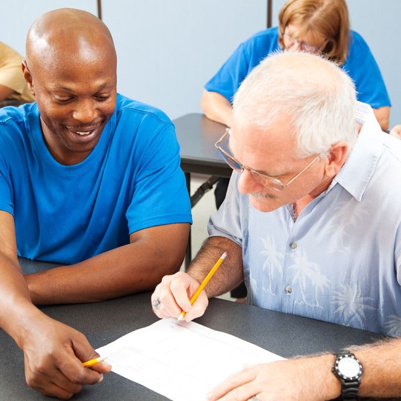 A man helping an elderly gentleman fill in a form